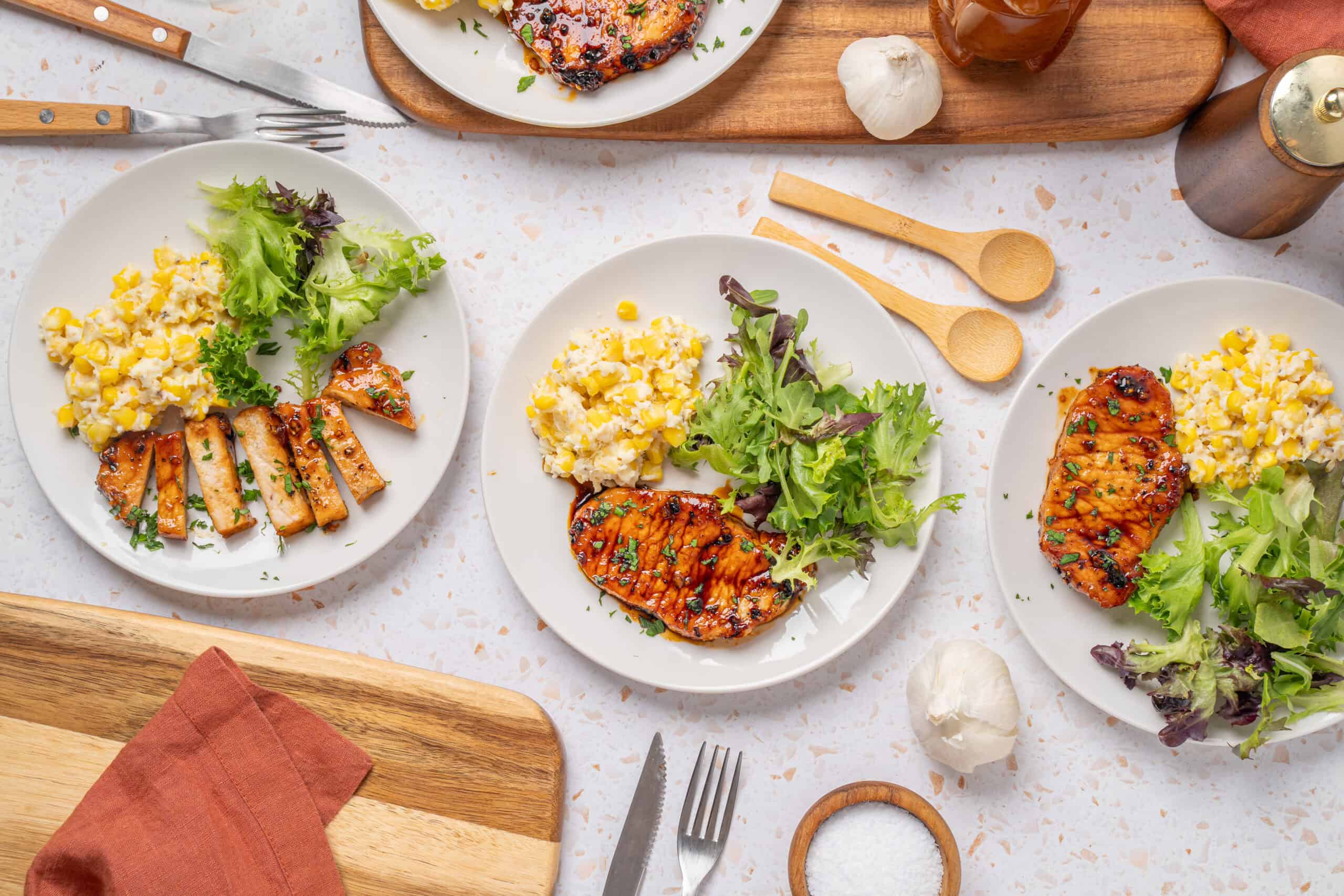 Grilled chicken breast with fresh side salad, corn salad, and mashed potatoes on white plates, served on a white textured surface for healthy dinner or lunch ideas.