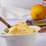 Creamy homemade lemon ice cream with grated lemon zest in a white ceramic bowl on a kitchen countertop. Healthy, refreshing dessert made with fresh citrus for summer.