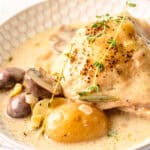 Juicy chicken thigh with creamy mushroom sauce, boiled potatoes, and fresh herbs on a textured white plate, perfect for hearty and flavorful dinner recipes.