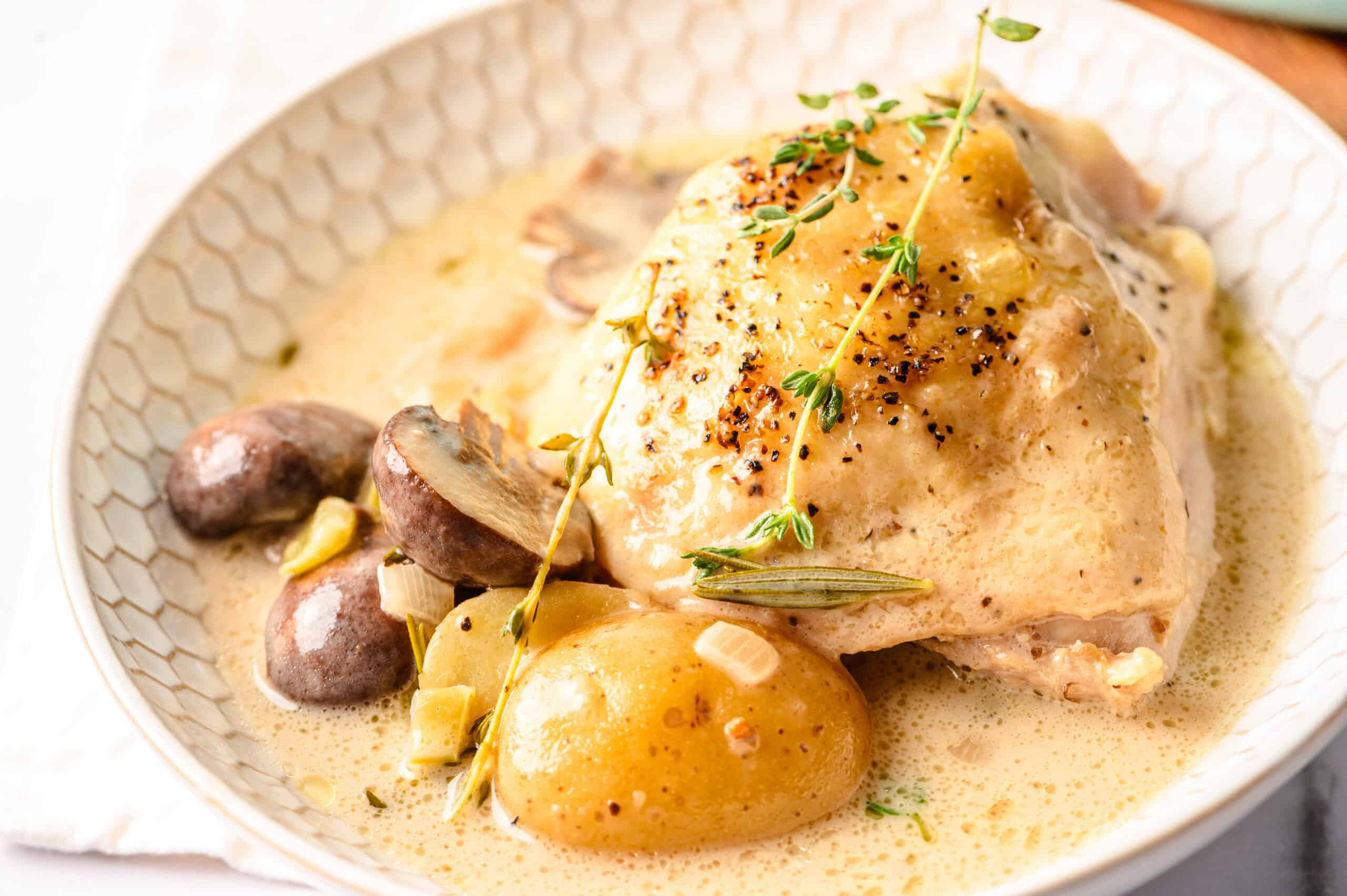 Juicy chicken thigh with creamy mushroom sauce, boiled potatoes, and fresh herbs on a textured white plate, perfect for hearty and flavorful dinner recipes.