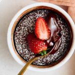 Rich chocolate lava cake topped with fresh strawberries and dusted with powdered sugar, served in a white ramekin, perfect for dessert.
