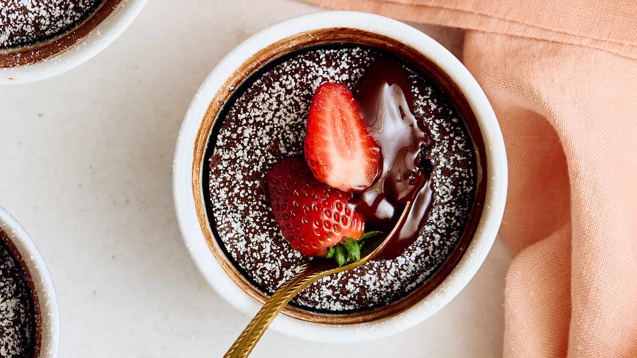 Rich chocolate lava cake topped with fresh strawberries and dusted with powdered sugar, served in a white ramekin, perfect for dessert.
