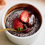 Rich chocolate lava cake topped with fresh strawberries and powdered sugar, served in a white ramekin for a decadent dessert.