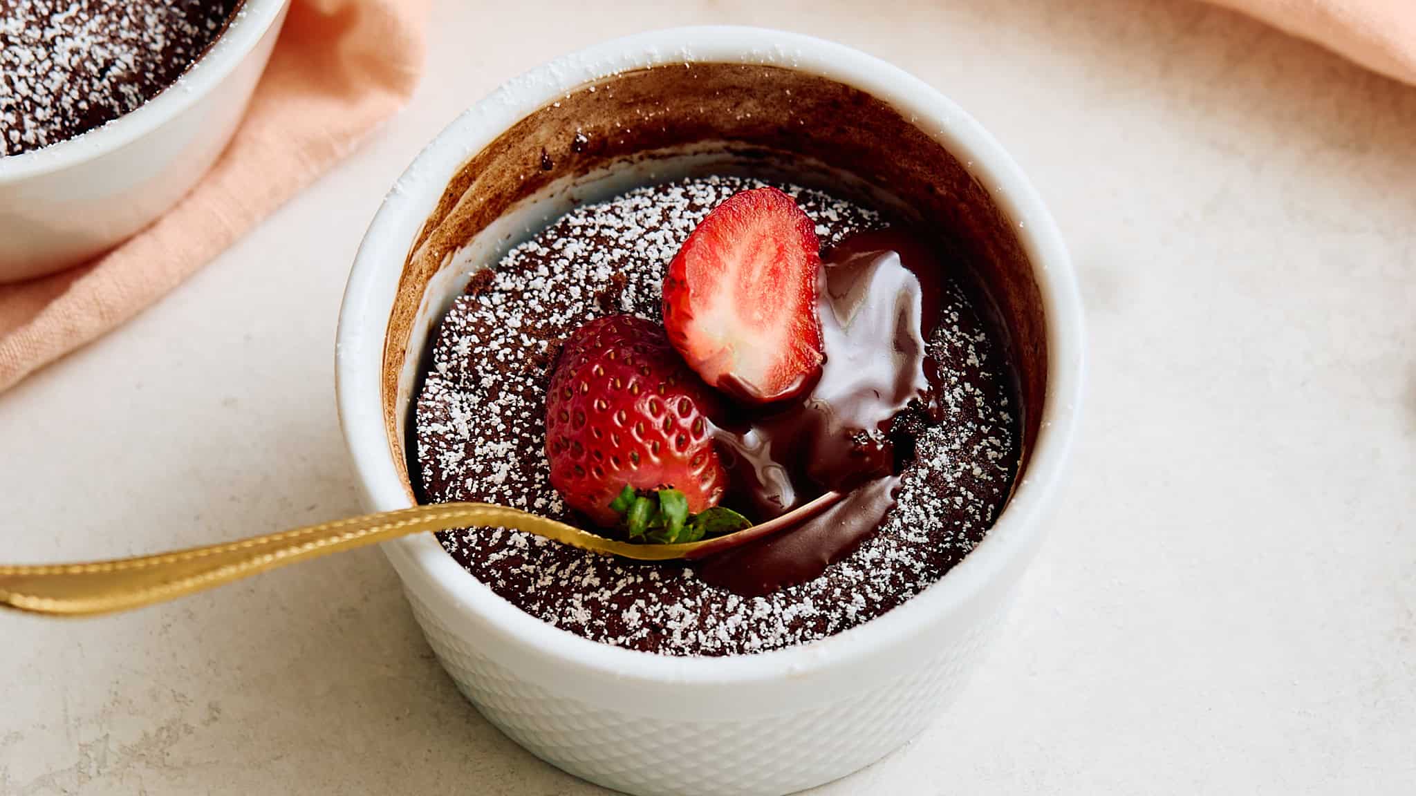Rich chocolate lava cake topped with fresh strawberries and powdered sugar, served in a white ramekin for a decadent dessert.