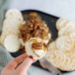 Soft cheese and pecans topped crackers with caramel honey on a black tray, served with a green cloth napkin for an elegant snack presentation.