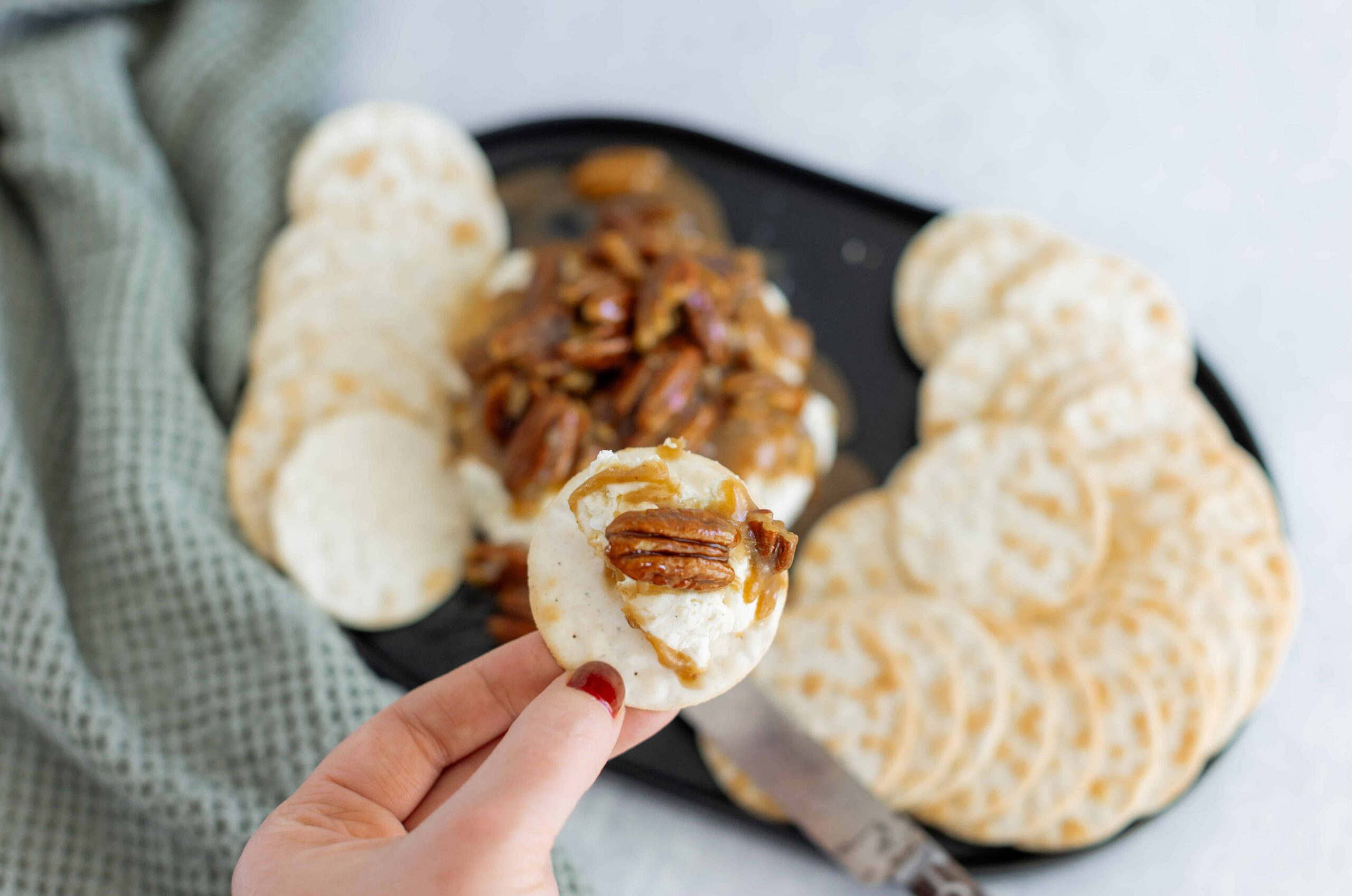 Soft cheese and pecans topped crackers with caramel honey on a black tray, served with a green cloth napkin for an elegant snack presentation.
