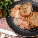 Tender grilled pork chops served with caramelized apples and onions on a black plate, fresh apples and parsley garnish, perfect for easy family dinner recipes.