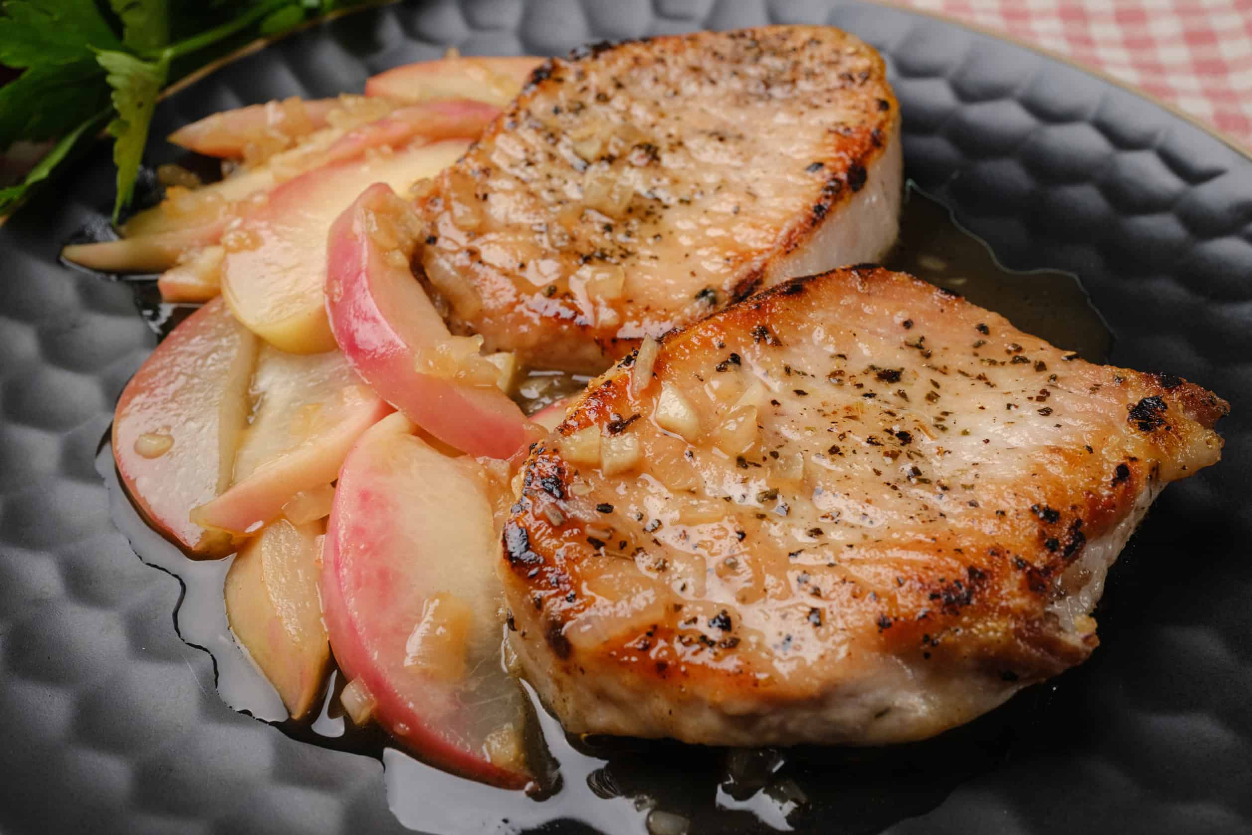 Juicy grilled pork chops with apples and caramelized onions served on a black plate. Perfect for a delicious and easy dinner recipe.
