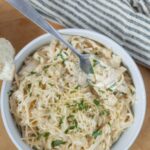 Creamy chicken and garlic shredded chicken salad in a white bowl garnished with fresh parsley, served with slices of toasted bread on a wooden table.