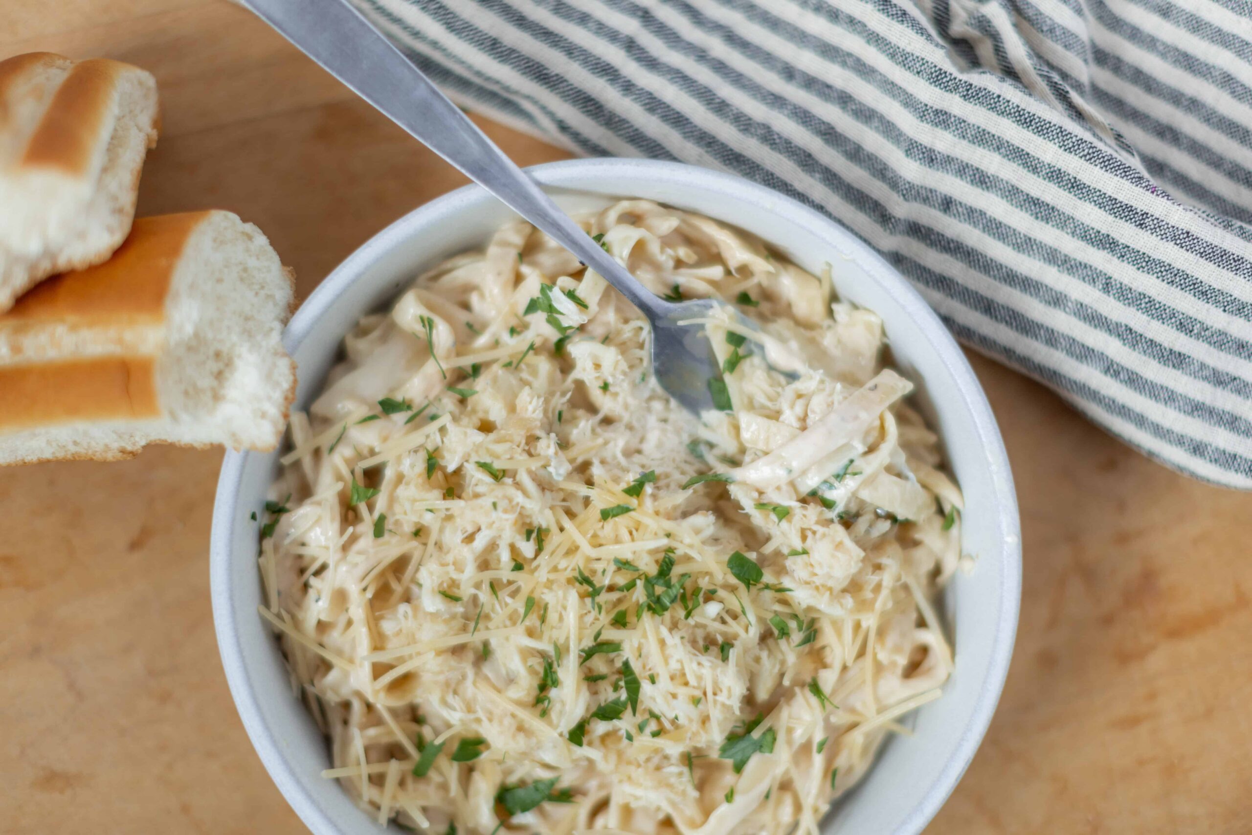 Creamy chicken and garlic shredded chicken salad in a white bowl garnished with fresh parsley, served with slices of toasted bread on a wooden table.