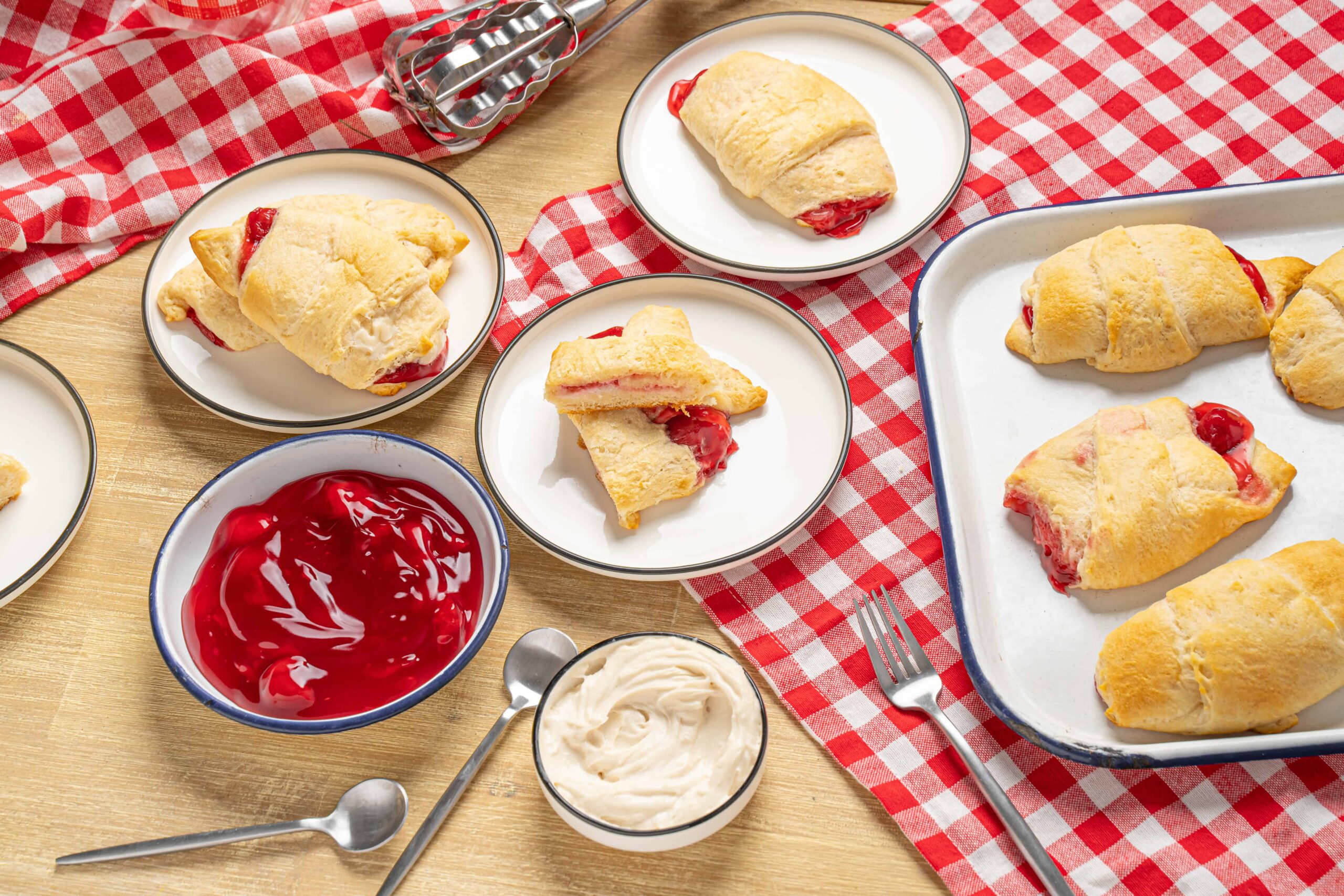 Flaky cherry turnovers with golden pastry crust served on white plates with cherry jam and whipped cream on a rustic wooden table; perfect homemade dessert.
