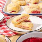 Flaky cherry-filled Danish pastry cut in half on a white plate with a red checkered tablecloth.
