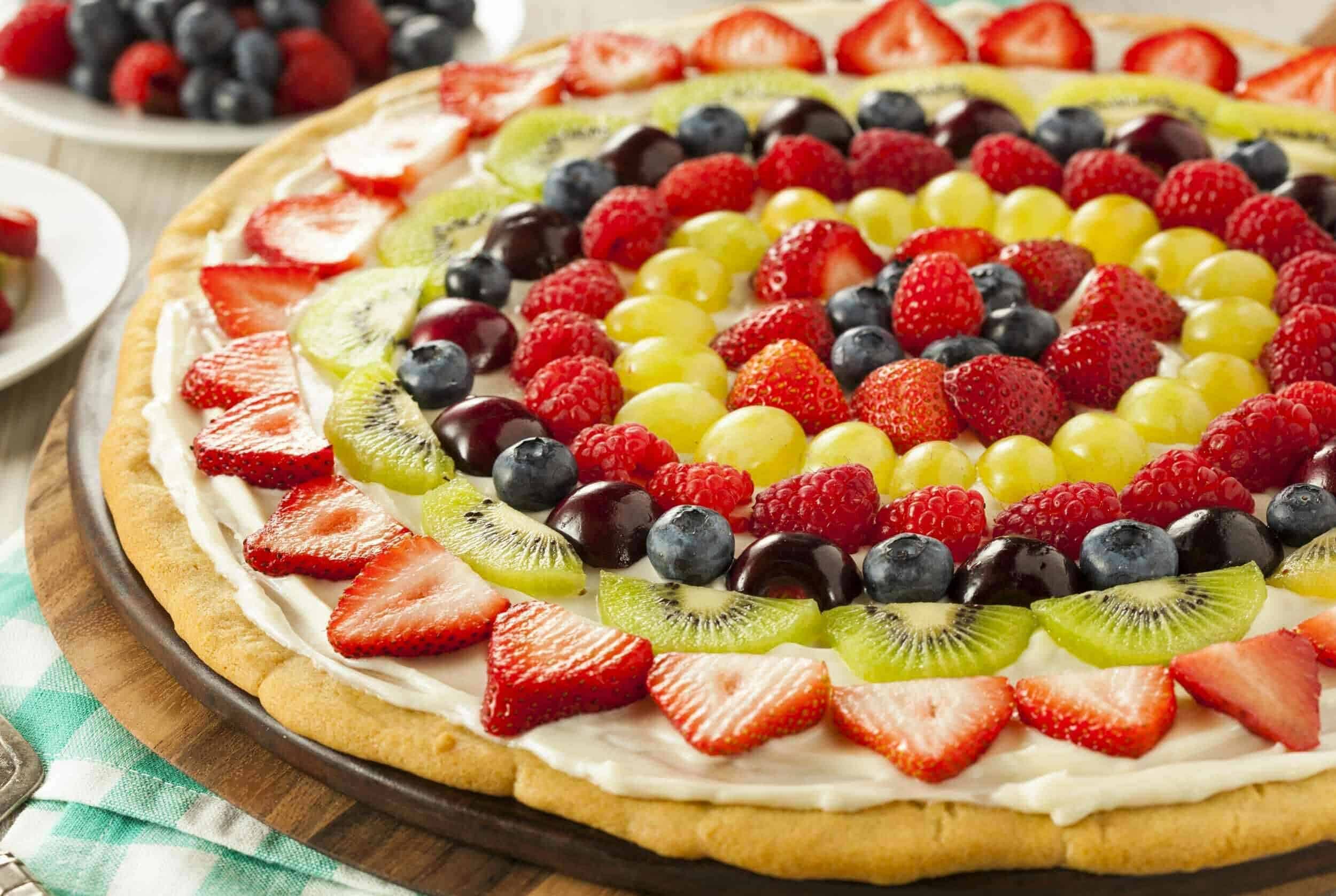 Fresh fruit pizza topped with strawberries, blueberries, kiwi, grapes, and raspberries on a wooden serving board for a vibrant, sweet, and colorful dessert.