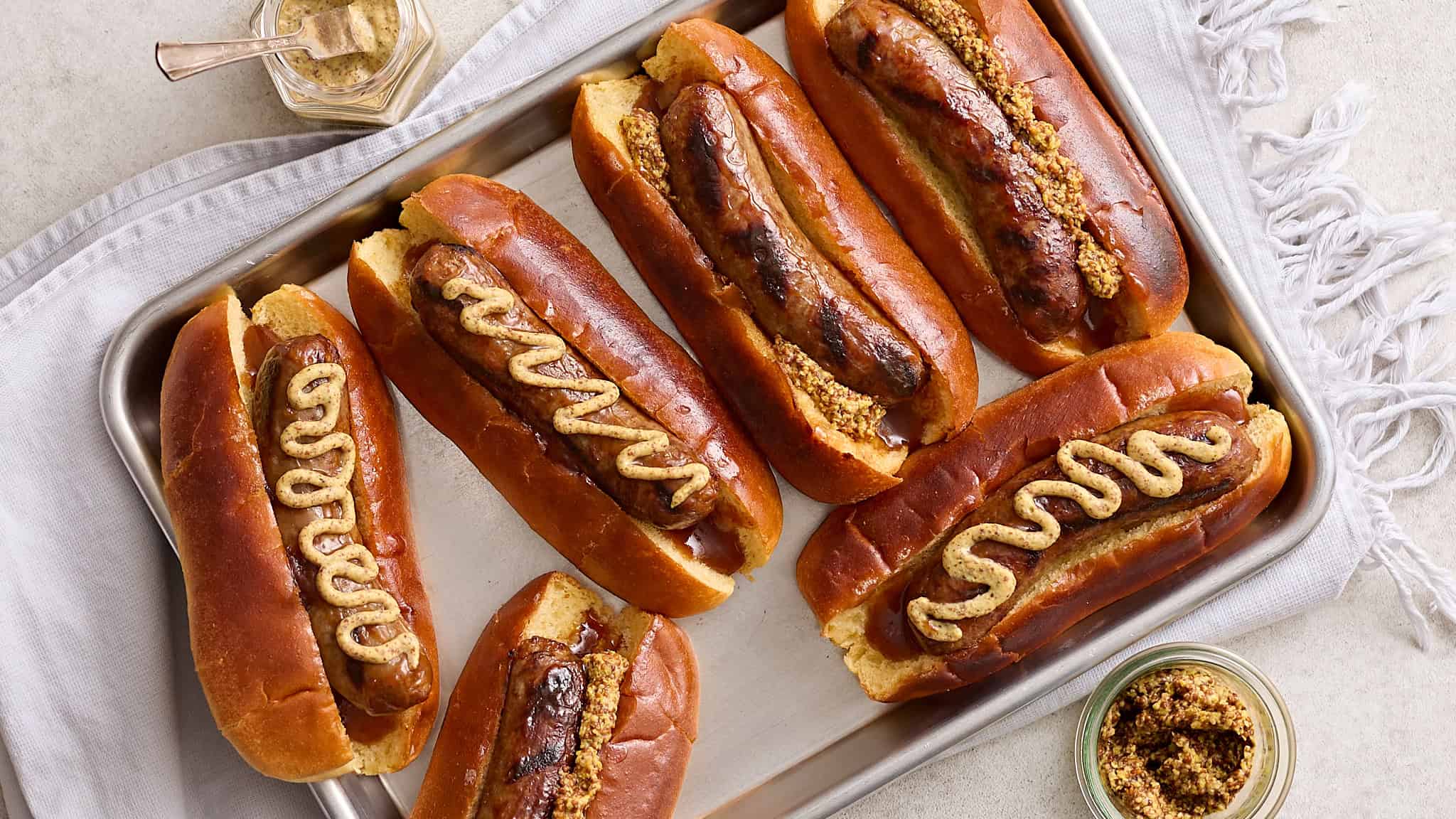 Savory hot dogs in soft buns with mustard and crushed toppings on a baking sheet; perfect for outdoor grilling and casual gatherings.