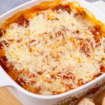Creamy baked Lasagna with melted cheese, tomato sauce, and ground meat served in a decorative baking dish on a wooden surface.