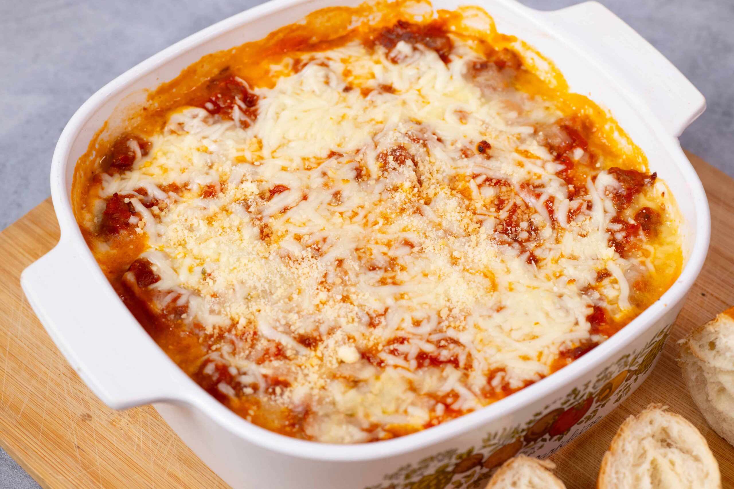 Creamy baked Lasagna with melted cheese, tomato sauce, and ground meat served in a decorative baking dish on a wooden surface.