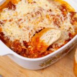 Creamy, homemade lasagna with layers of rich tomato sauce, melted cheese, and tender pasta, served in a decorative baking dish with freshly sliced bread on the side. Perfect for family dinners and comfort food lovers.