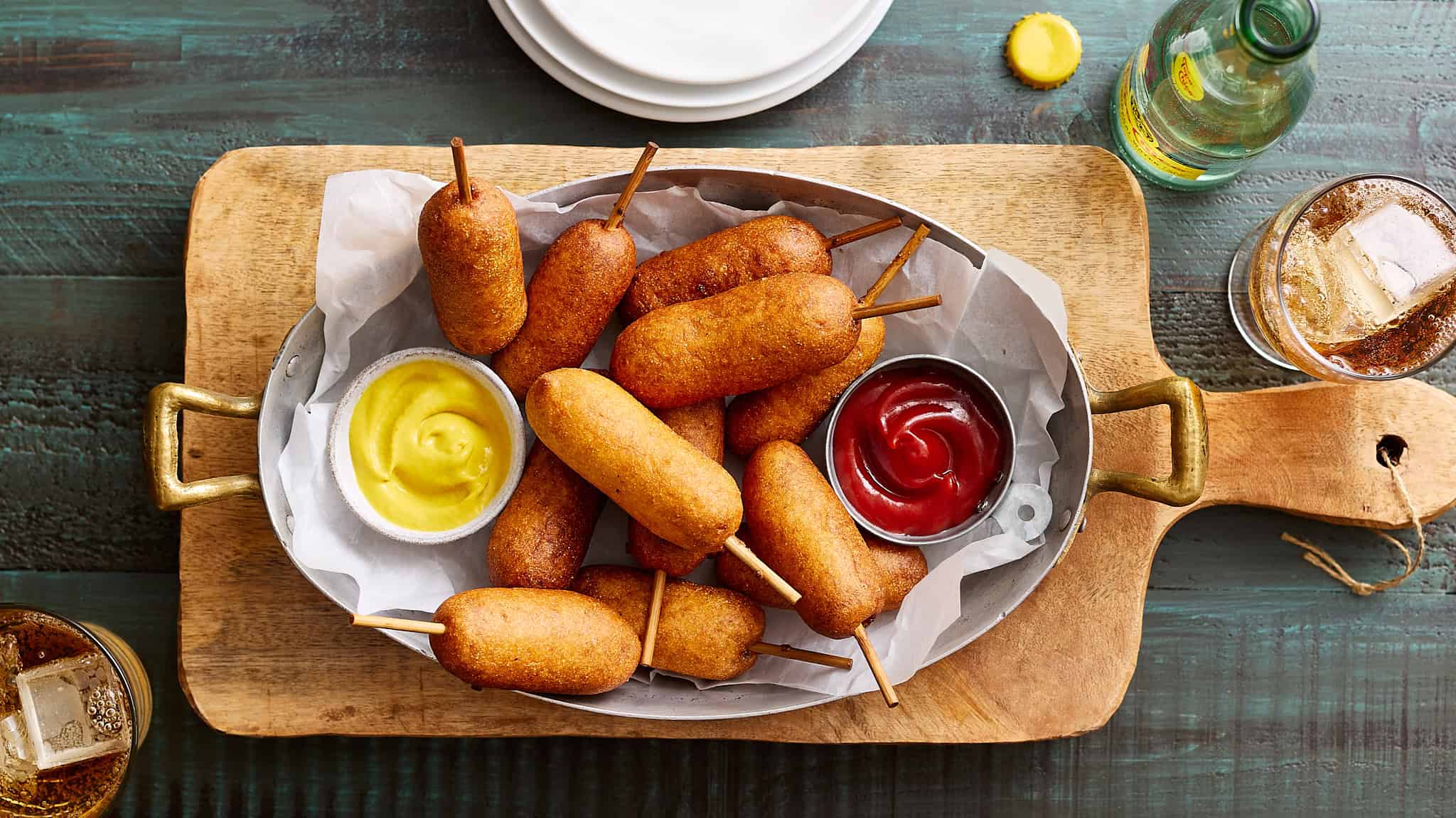 Crispy fried corn dogs served with mustard and ketchup dipping sauces on a wooden tray.