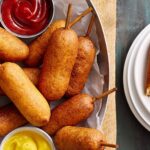 Crispy mozzarella sticks served with ketchup and mustard dipping sauces on a rustic wooden tray, perfect for appetizer or snack ideas, highlighting comfort food, crunchy exterior, and cheesy interior.