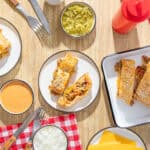 Delicious beef and cheese burritos with sesame seed topping served with dipping sauces on a wooden table.