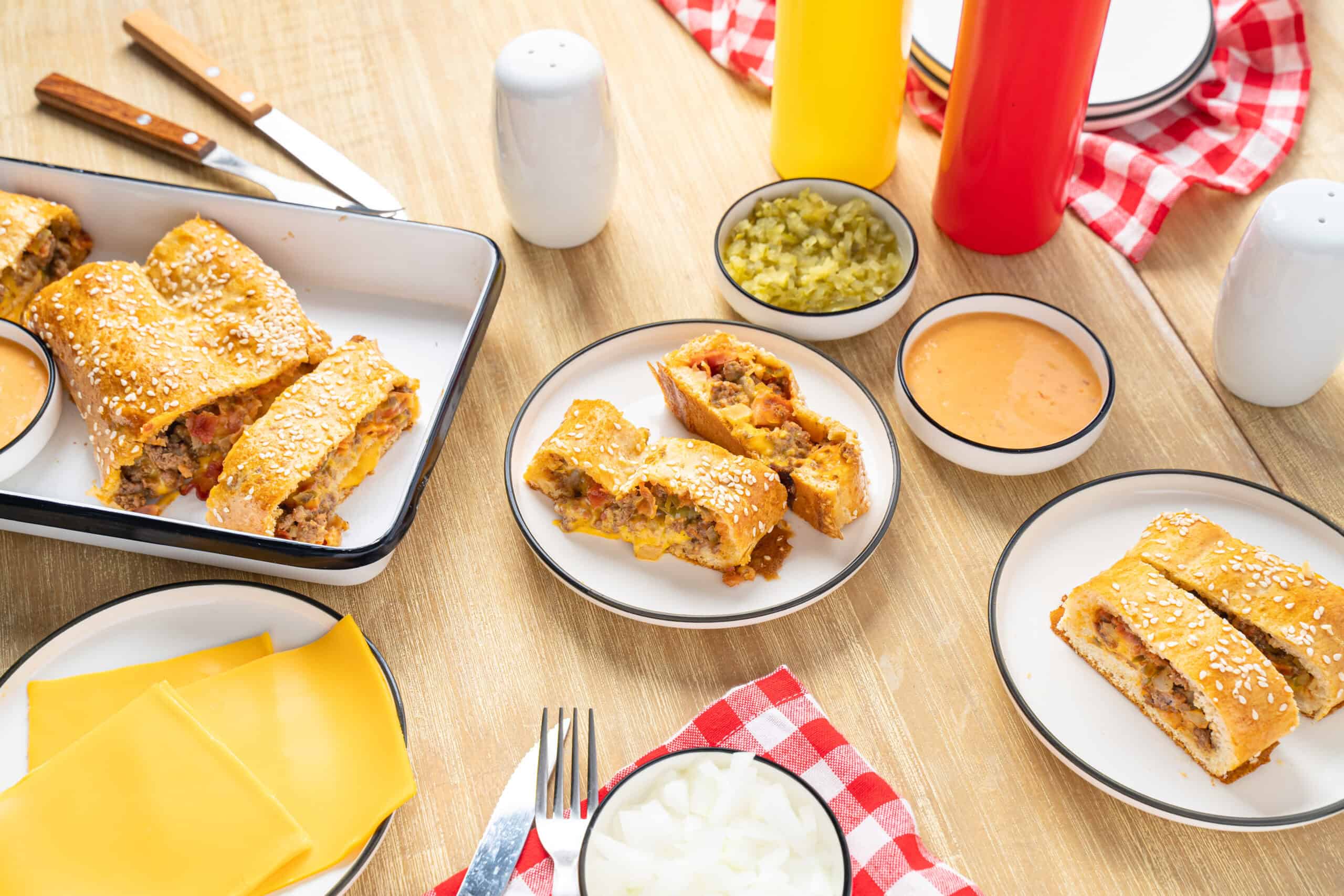 Golden baked beef and cheese eggrolls sliced and served with dipping sauces, fresh vegetables, and condiments on a wooden table, perfect for appetizer or snack.