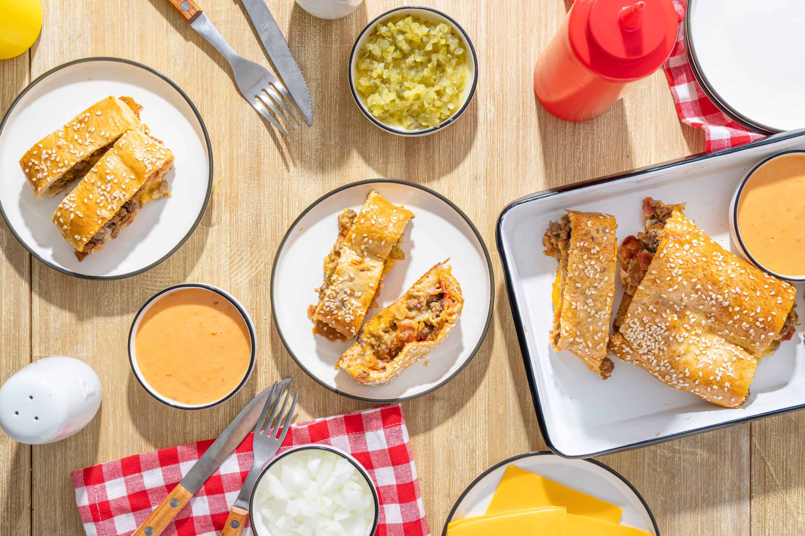 Delicious beef and cheese burritos with sesame seed topping served with dipping sauces on a wooden table.