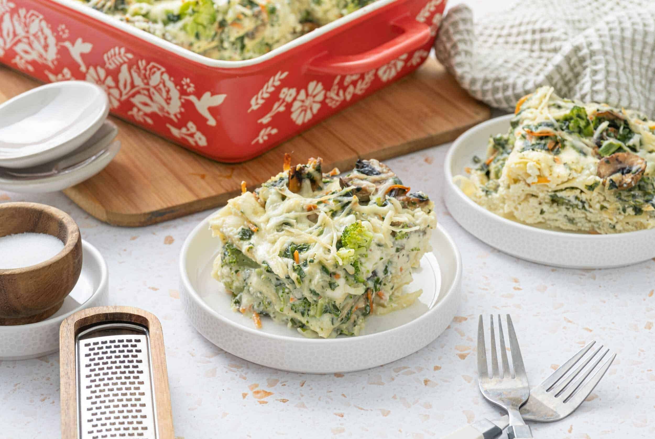 Creamy vegetable and cheese casserole with broccoli, spinach, and mushrooms on white plates. Perfect for a healthy, hearty meal or side dish, featuring a rich, cheesy sauce and fresh ingredients.