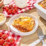 Succulent homemade lasagna with layers of cheese, meat sauce, and pasta, served with fresh cherry tomatoes, grated Parmesan, and baked in a white ceramic dish for a comforting Italian meal.