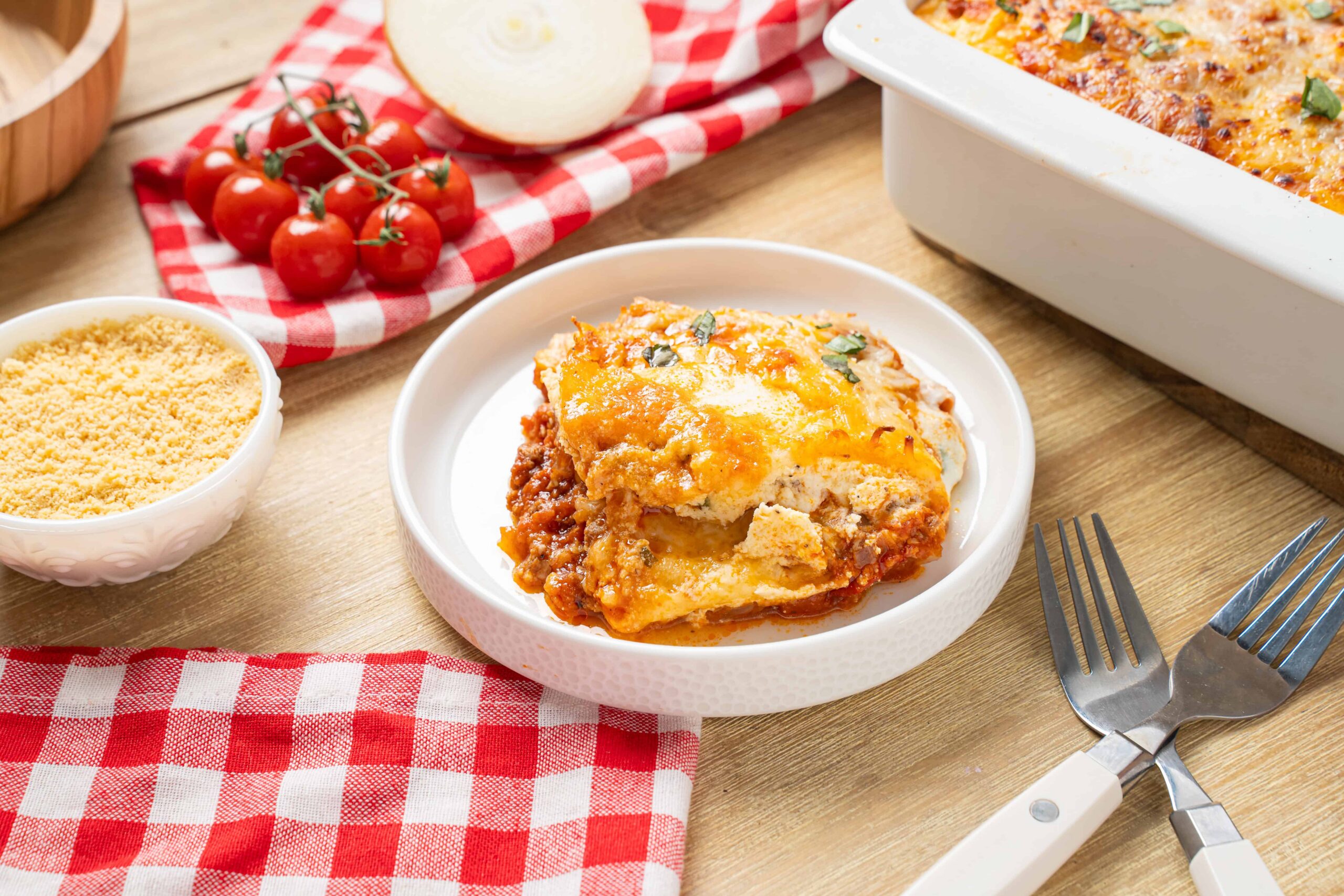 Creamy lasagna with melted cheese and savory meat sauce served in a white bowl on a wooden table, surrounded by fresh ingredients and kitchen utensils, perfect for a hearty Italian meal.