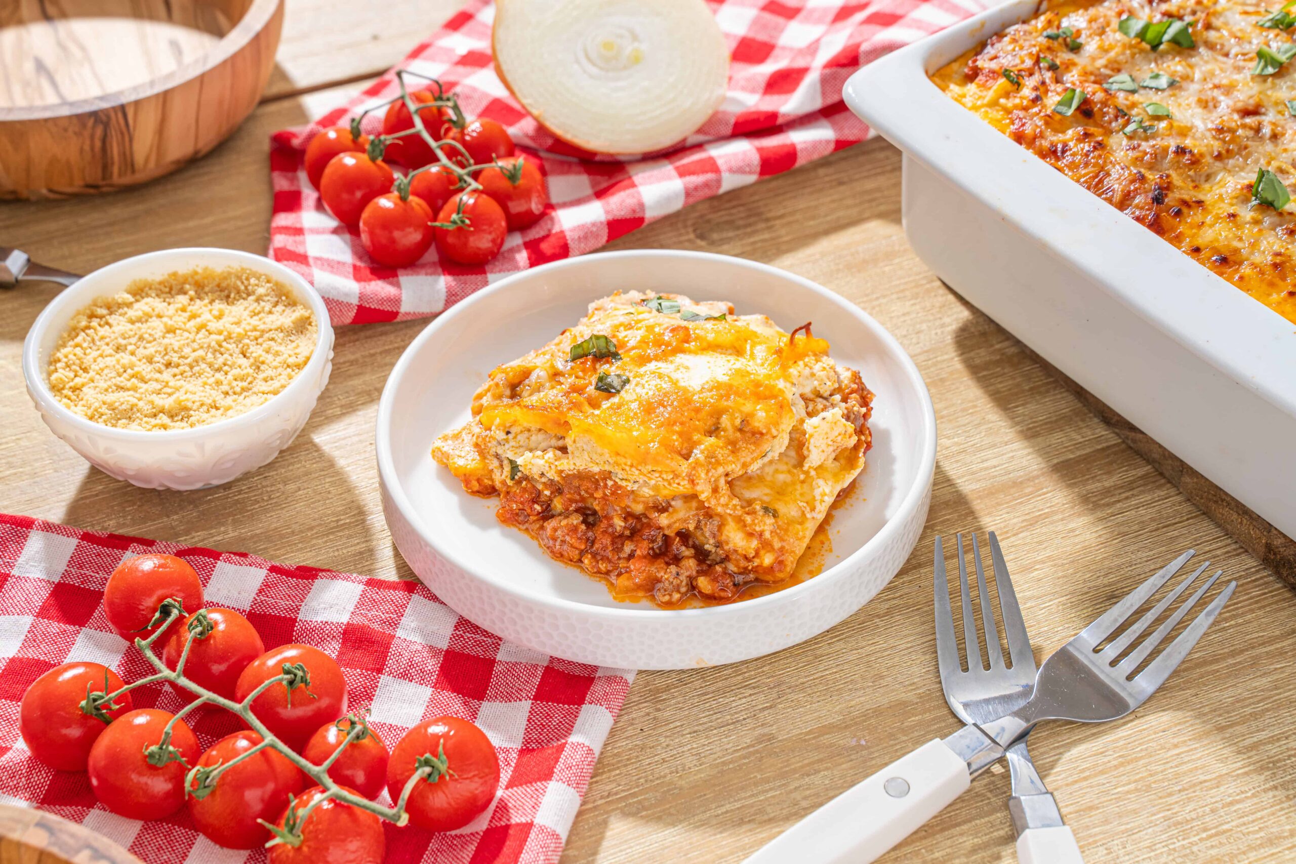 Succulent homemade lasagna with layers of cheese, meat sauce, and pasta, served with fresh cherry tomatoes, grated Parmesan, and baked in a white ceramic dish for a comforting Italian meal.