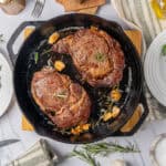 Juicy pan-seared ribeye steaks garnished with fresh rosemary on a cast iron skillet, served alongside vibrant garden salads, garlic cloves, and a bottle of olive oil for easy, delicious dinner ideas.