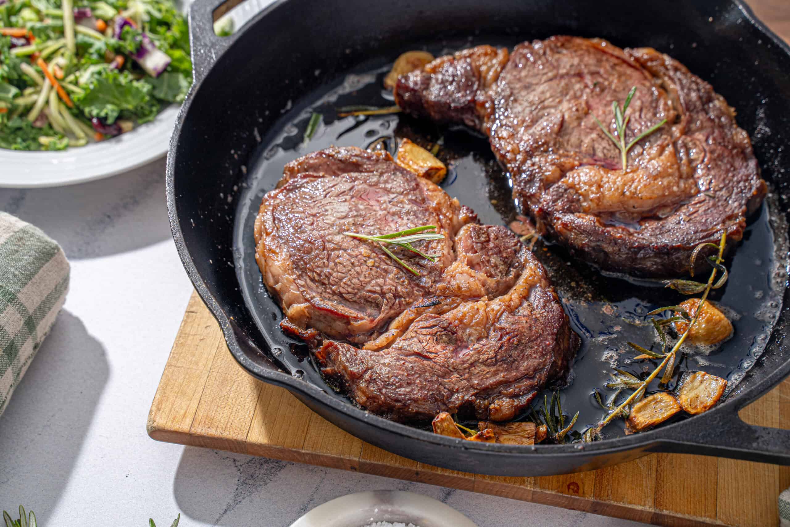 Juicy, seasoned steaks cooking in a cast iron skillet with garlic and herbs, perfect for a flavorful dinner.