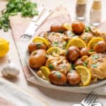 Juicy roasted chicken with lemon slices, baby potatoes, and fresh herbs on a white serving platter, served for a delicious homemade dinner or special occasion meal.