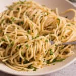 Creamy garlic spaghetti with fresh parsley in a white bowl, served with a fork for a delicious Italian pasta dish. Perfect for quick weeknight dinners or cozy home meals.
