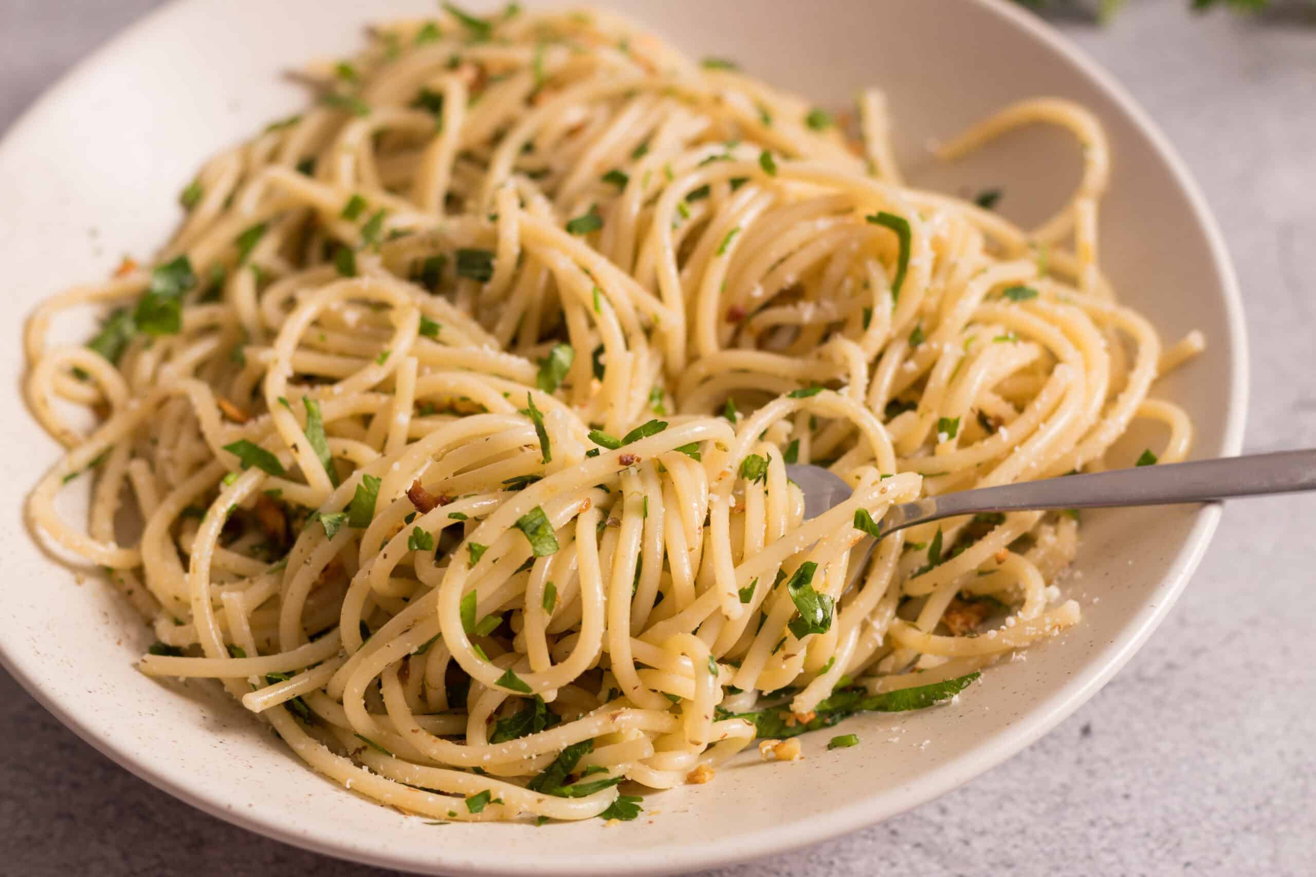 Creamy garlic spaghetti with fresh parsley in a white bowl, served with a fork for a delicious Italian pasta dish. Perfect for quick weeknight dinners or cozy home meals.