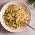 Creamy garlic butter spaghetti with fresh parsley, served in a white bowl on a rustic gray surface, garnished with chopped herbs for a delicious, quick, and easy pasta recipe.