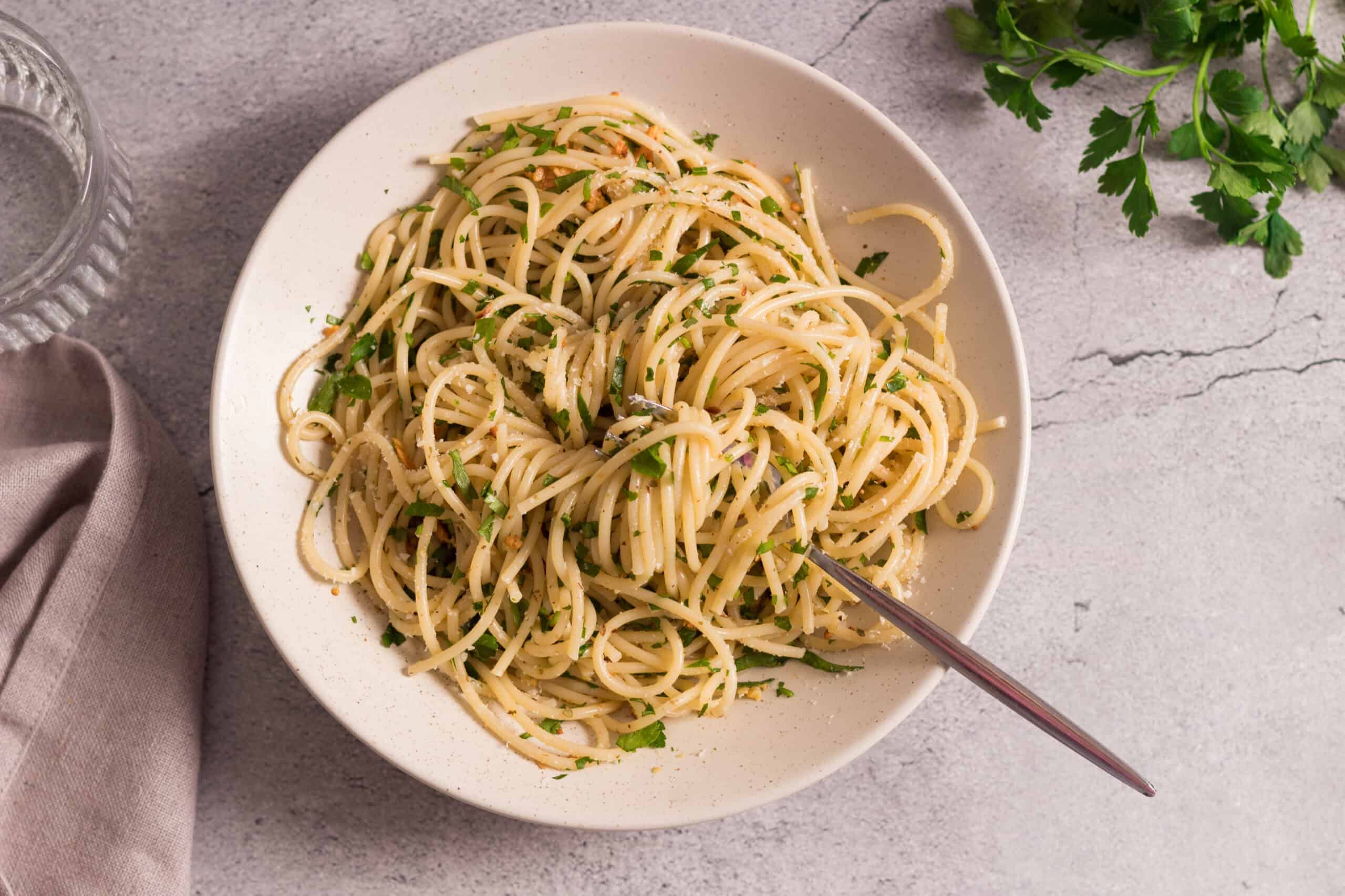 Creamy garlic butter spaghetti with fresh parsley, served in a white bowl on a rustic gray surface, garnished with chopped herbs for a delicious, quick, and easy pasta recipe.