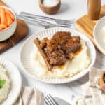 Slow cooker beef short ribs served over creamy mashed potatoes with side of glazed carrots and black pepper. Perfect comfort food recipe for family dinners and weekend meals.