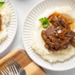 Tender beef short ribs with savory onion gravy served over creamy mashed potatoes, garnished with fresh parsley - perfect comfort food recipe.