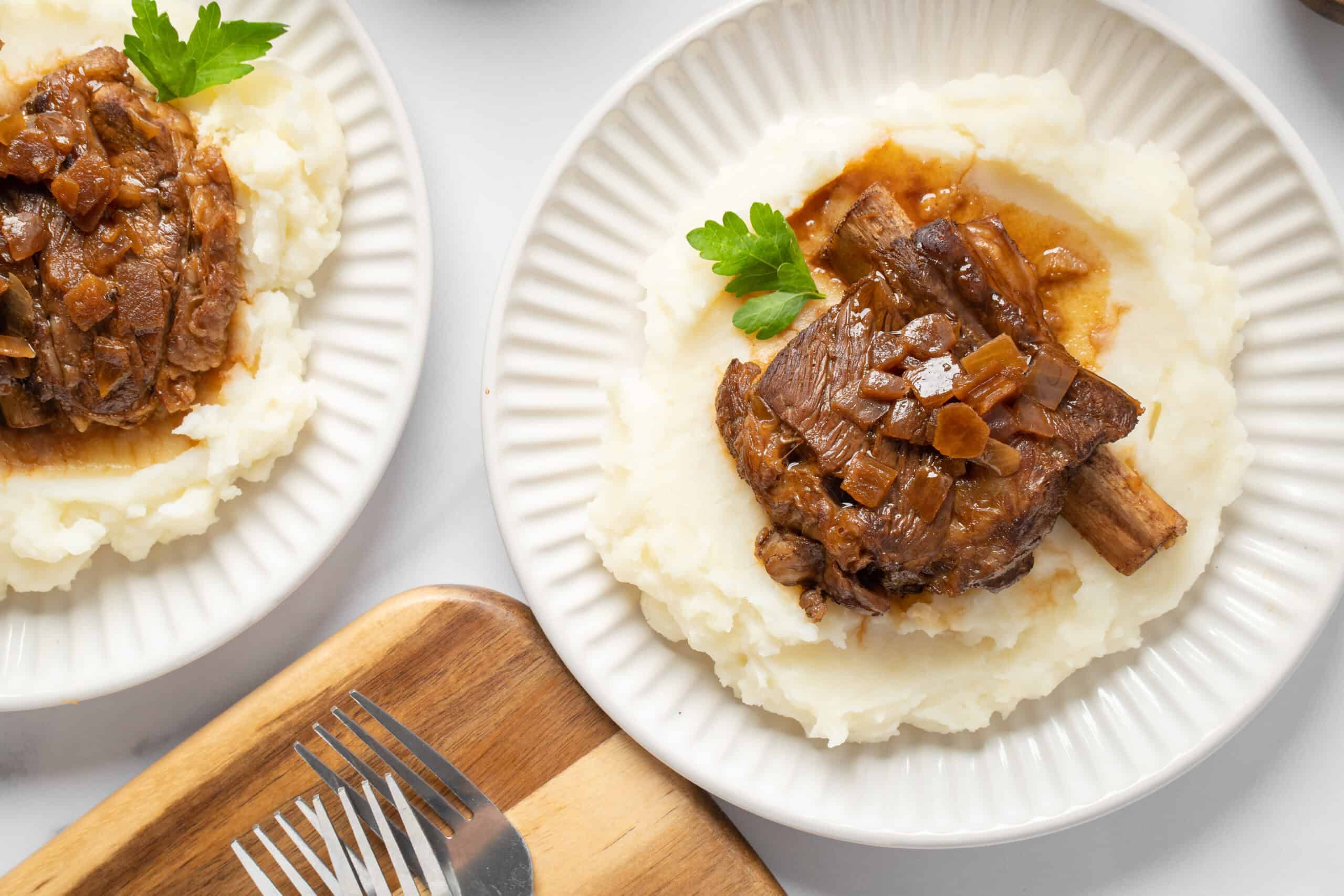 Tender beef short ribs with savory onion gravy served over creamy mashed potatoes, garnished with fresh parsley - perfect comfort food recipe.