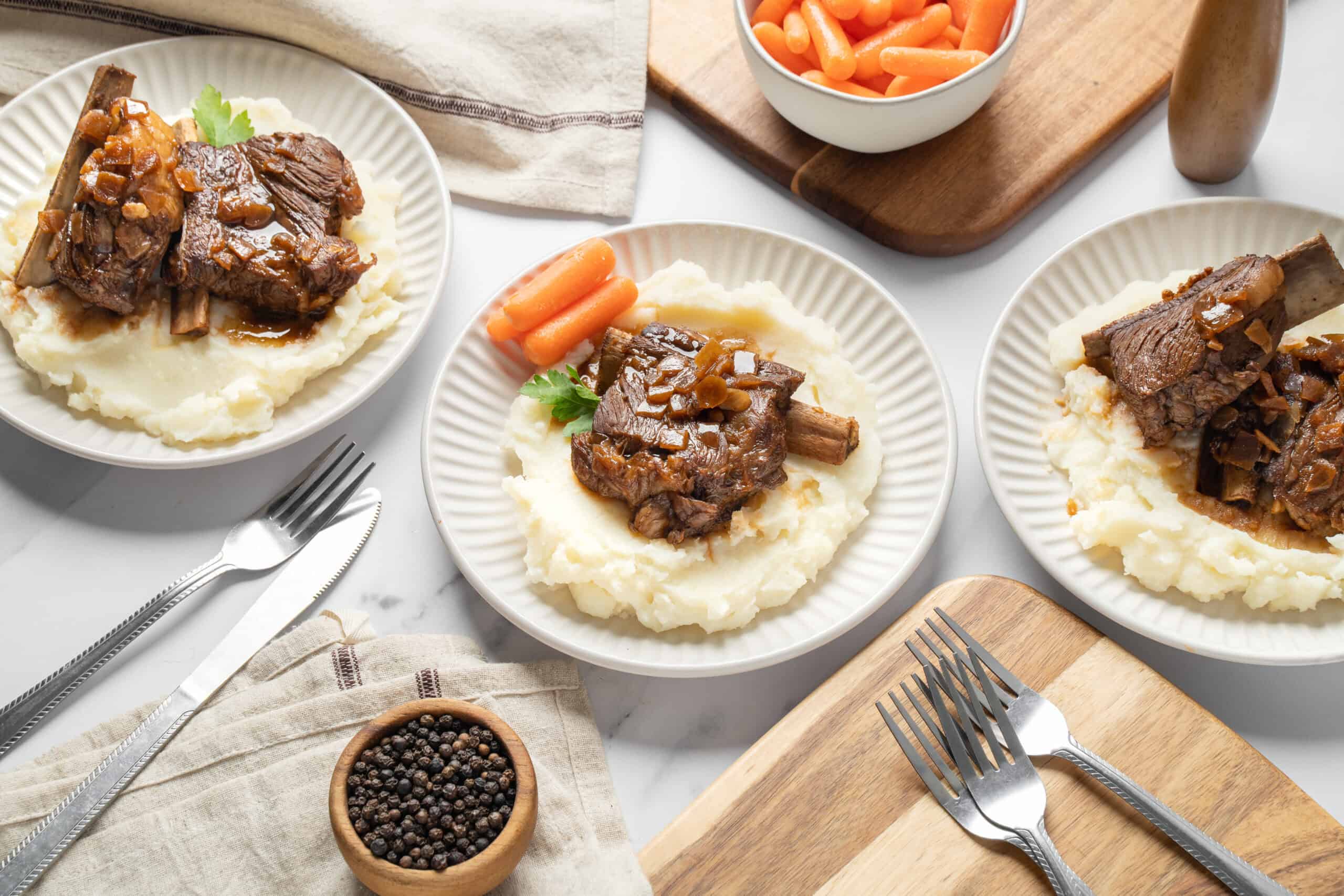 Savory beef stew with vegetables served over creamy mashed potatoes on white plates for a hearty comfort meal.