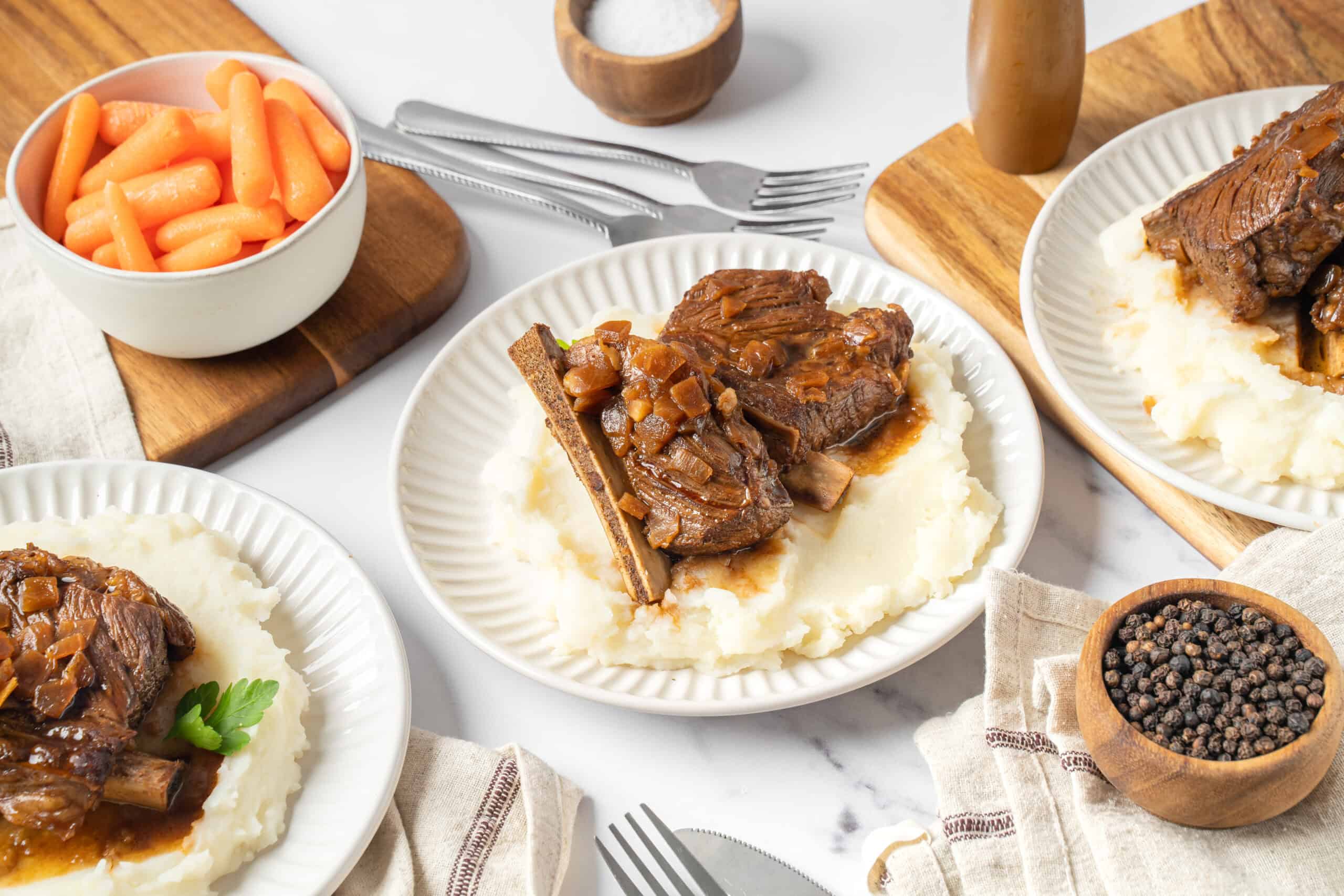 Slow cooker beef short ribs served over creamy mashed potatoes with side of glazed carrots and black pepper. Perfect comfort food recipe for family dinners and weekend meals.
