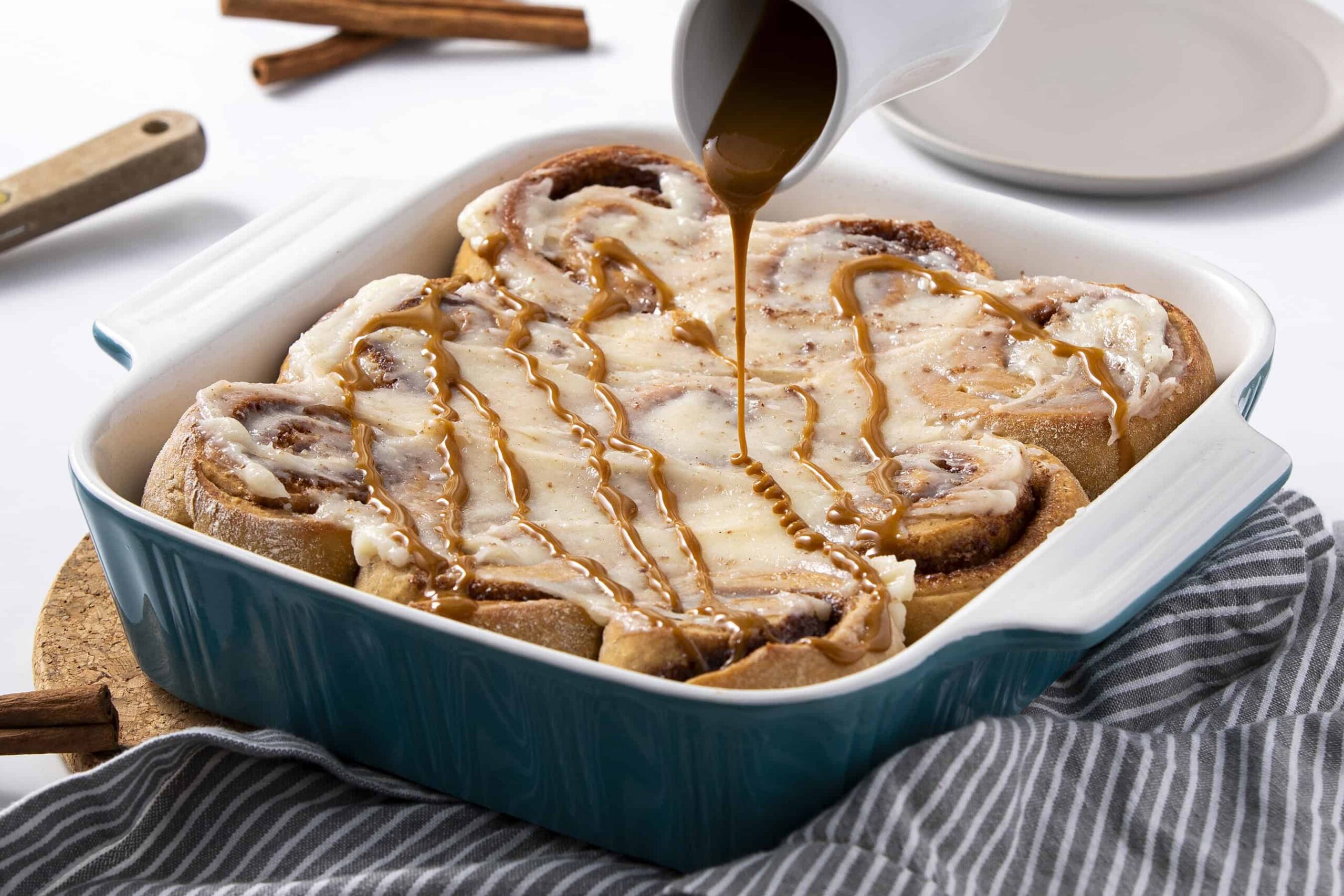 Creamy cinnamon roll casserole topped with melted cheese, drizzled caramel sauce, and baked to perfection, served in a blue baking dish. Perfect breakfast or dessert for cozy mornings or special occasions.
