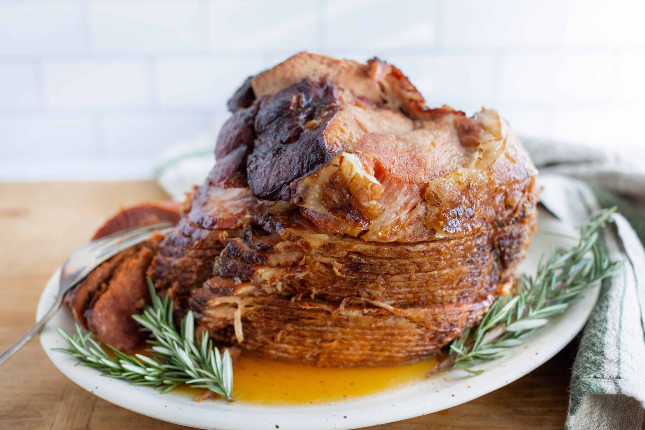 Juicy baked ham with a caramelized glaze garnished with fresh rosemary on a white platter. Perfect for holiday dinner recipes and festive celebrations.