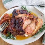 Braised pork roast with caramelized exterior and tender interior served on a white plate with fresh herbs and a fork, showcasing hearty comfort food perfect for family dinners or special occasions.