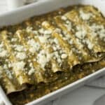 Seasoned meat and cheese enchiladas baked in a white casserole dish with melted cheese topping.