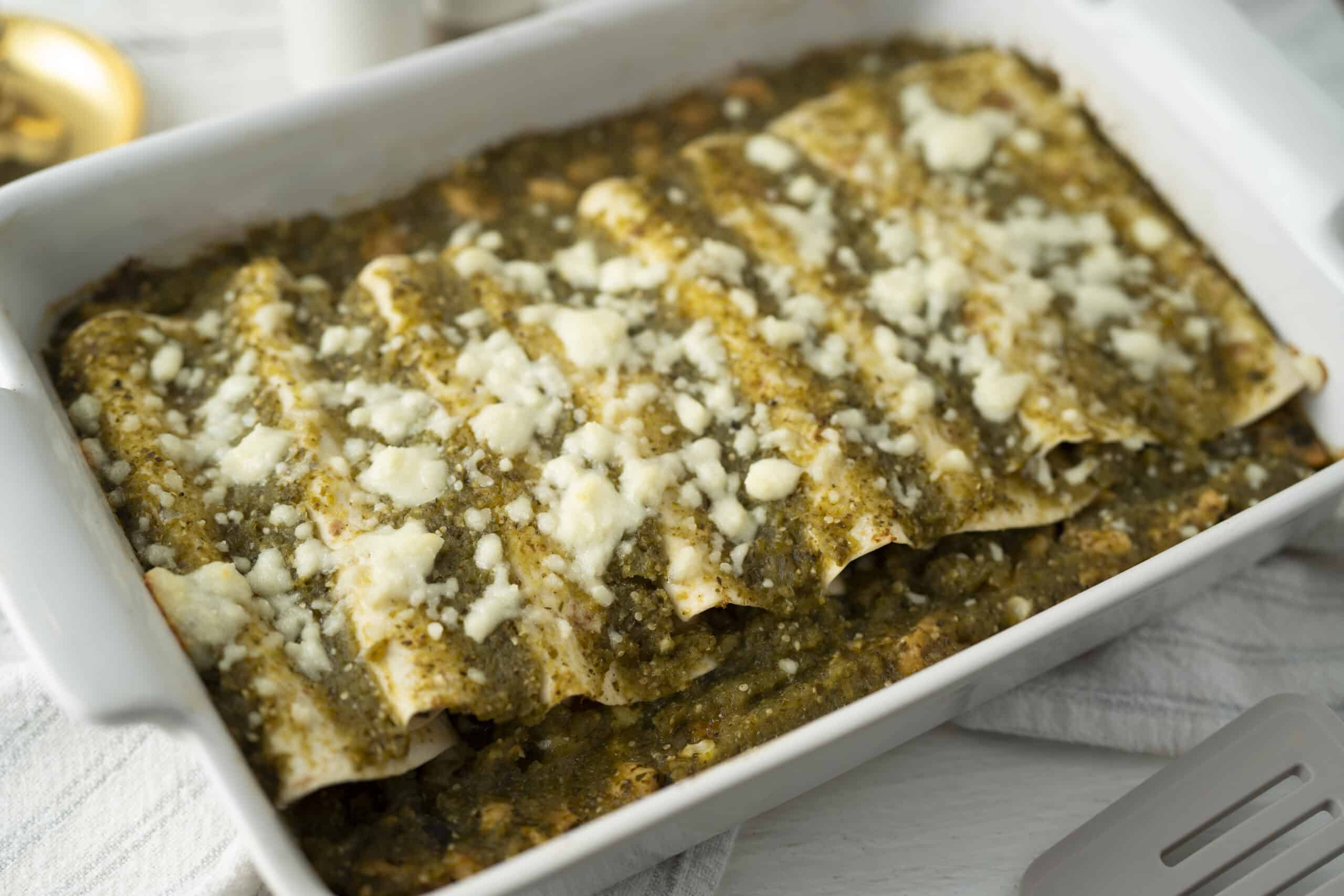 Seasoned meat and cheese enchiladas baked in a white casserole dish with melted cheese topping.