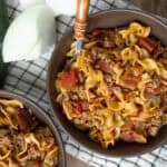 Savory beef and vegetable pasta dish in brown bowls, garnished with fresh zucchini and black pepper on a checkered cloth.