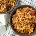 Savory ground beef and pasta skillet with tomatoes, onions, and green peppers in brown bowls on a checkered cloth, topped with fresh mozzarella cheese, perfect for quick dinner recipes.