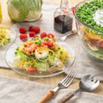 Fresh homemade chef salad with eggs, tomatoes, green peas, cheese, and lettuce served on glass plates; colorful and healthy dinner option.